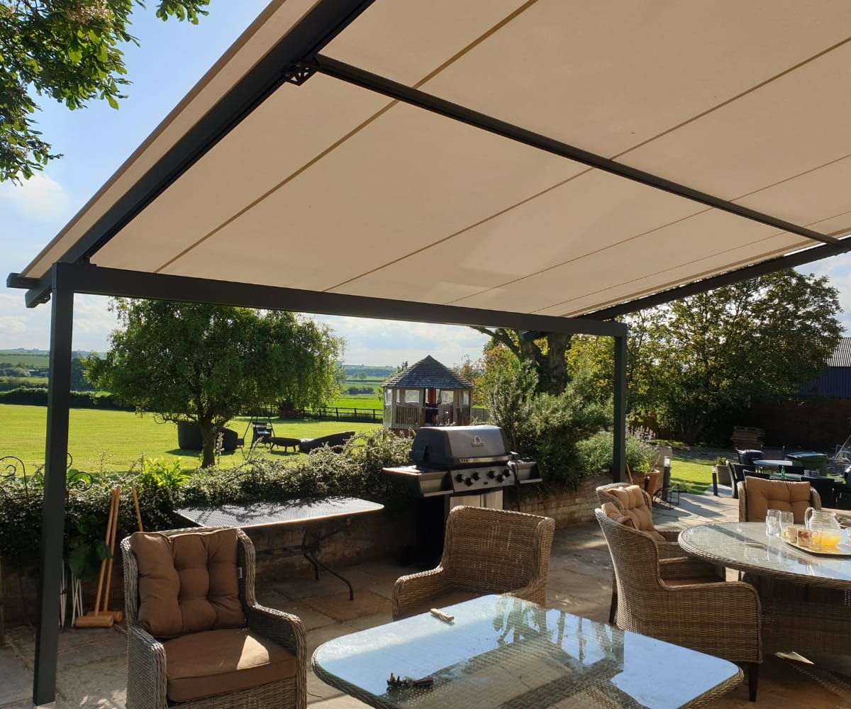 A pergola over a decking with a view of a lawn.