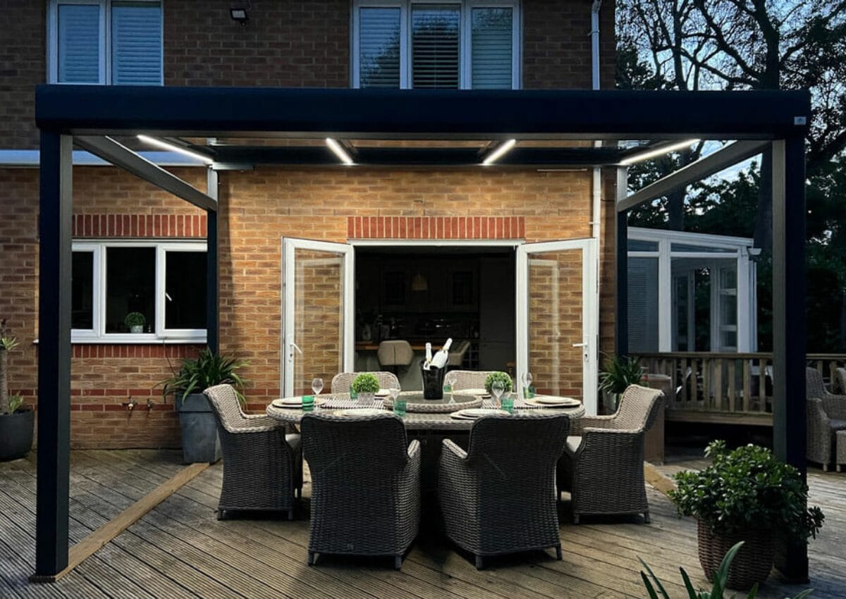 A dining table outside under a VELARIUM retractable glass awning in the evening.
