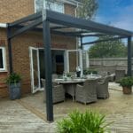 A VELARIUM retractable glass awning over a dining table in a luxurious garden