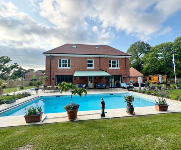Bespoke garden awning installed over a patio area by a pool, outside a large red-brick home