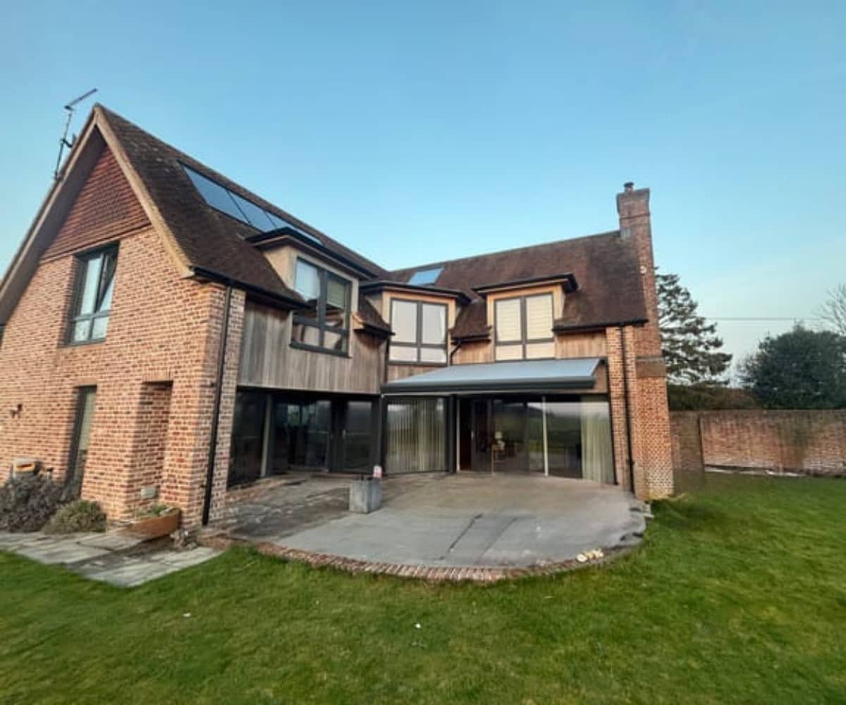 Modern bespoke awning fitted to a large house with brick and timber cladding under a clear blue sky