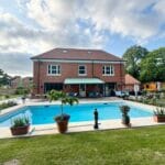 Bespoke garden awning installed over a patio area by a pool, outside a large red-brick home