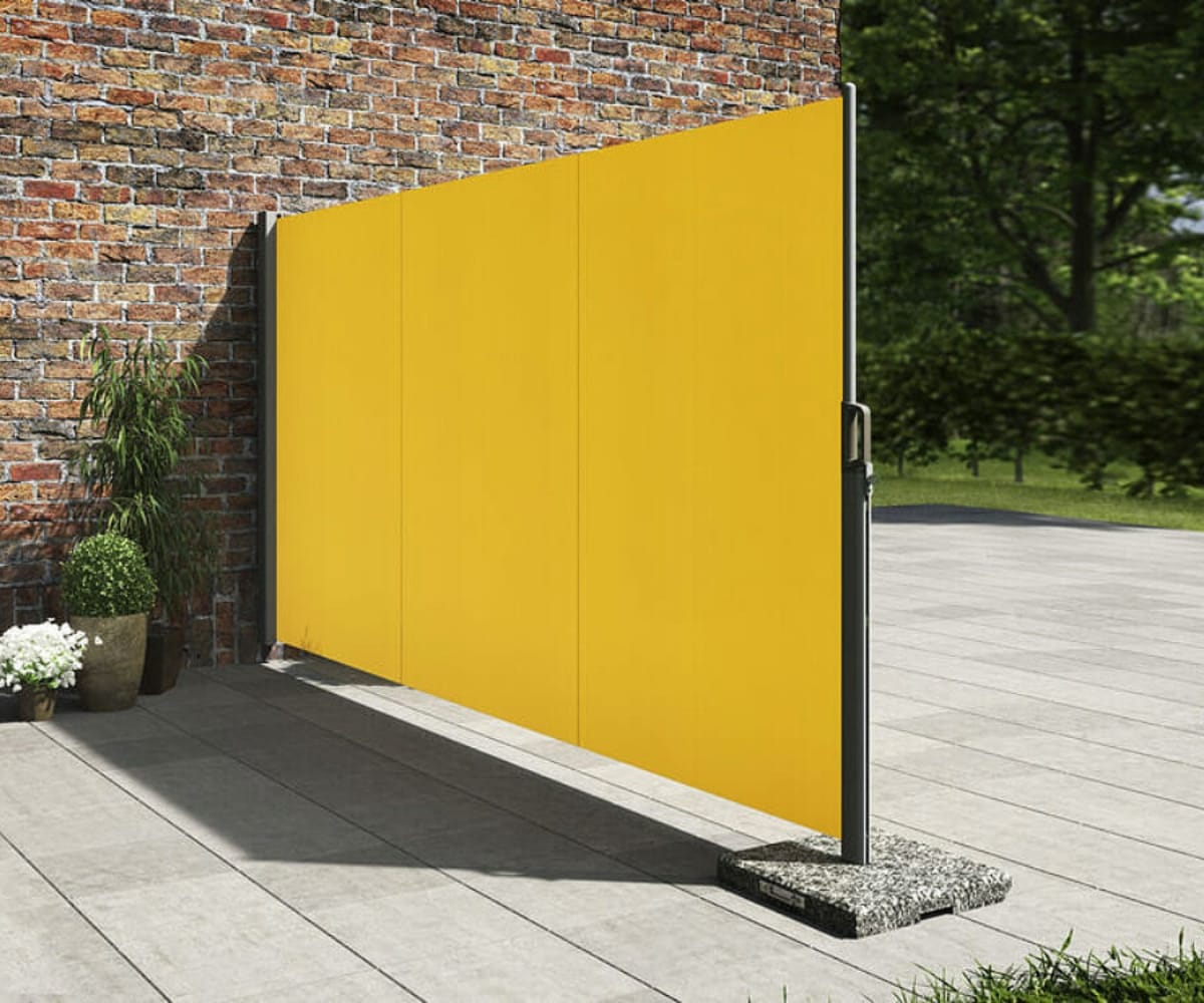 Freestanding yellow privacy blind from The Great British Awning and Blinds Company, positioned on a patio next to a brick wall