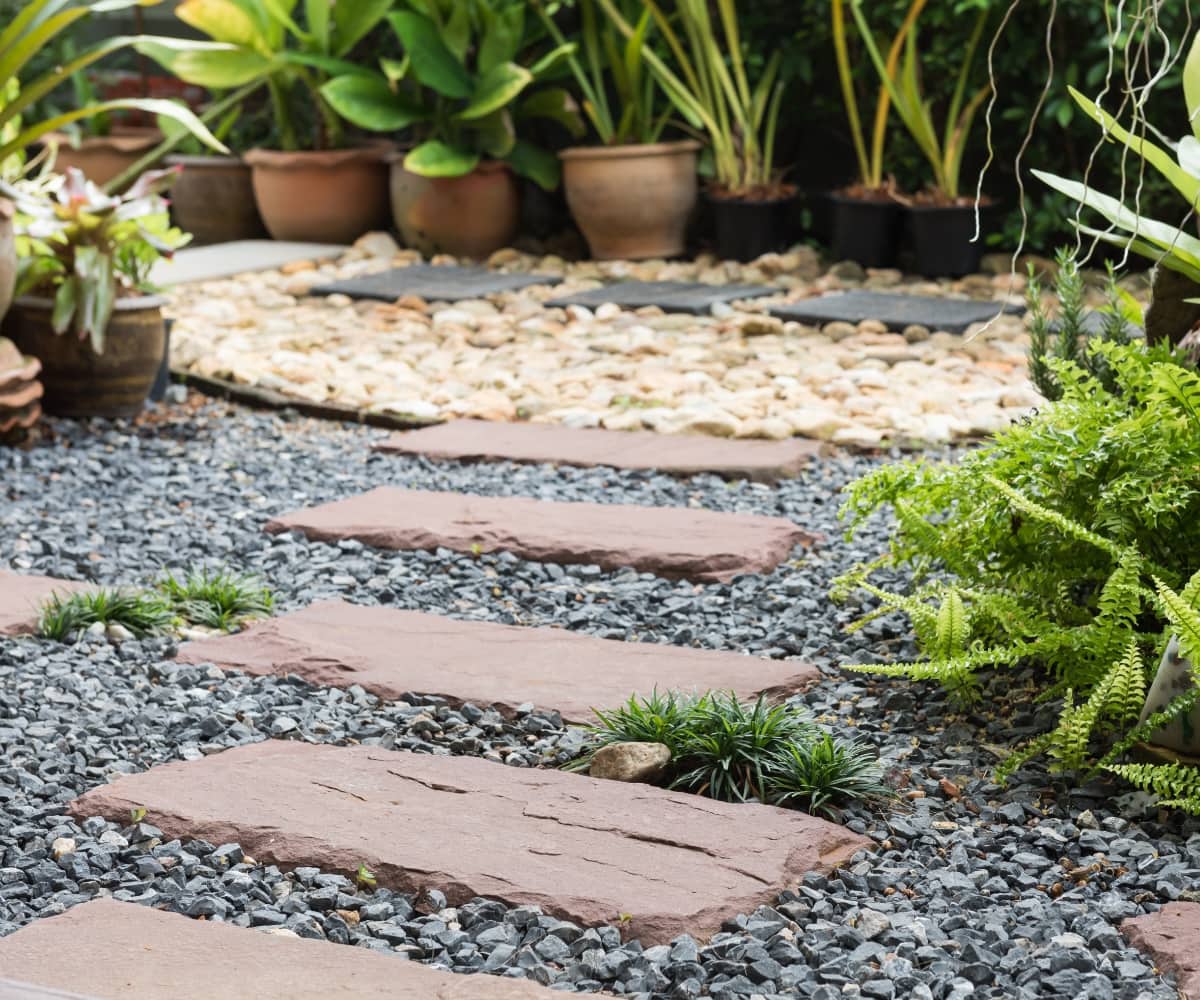 Stone pathway with gravel, plants, and pots in landscaped garden