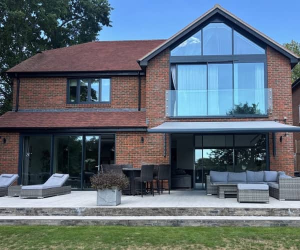 Stylish red-brick home with a large patio, lounge furniture, and retractable awning creating a shaded outdoor workspace.