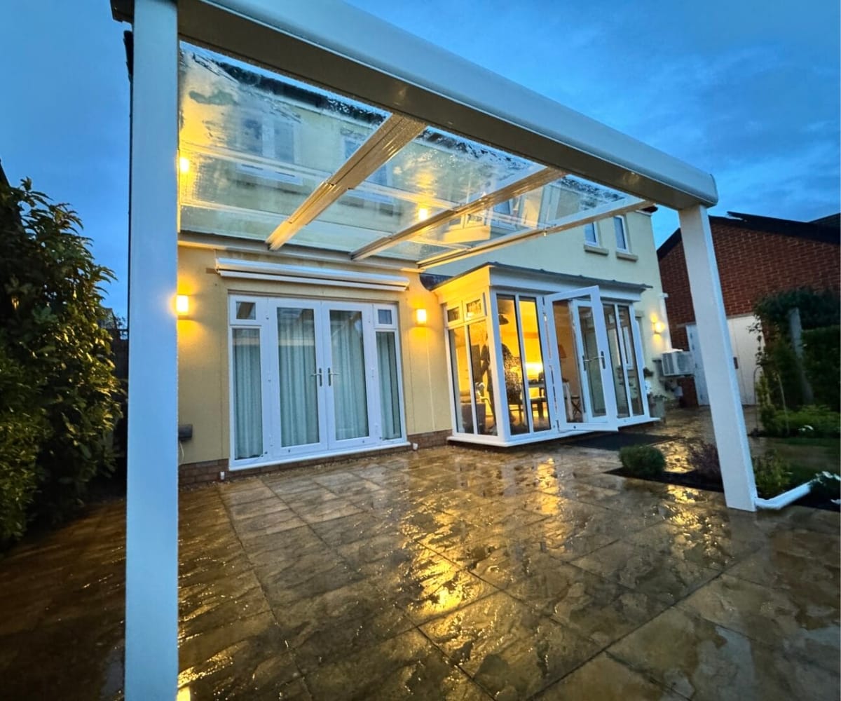 glass veranda or awning: Glass veranda attached to a UK home at dusk, with integrated lighting and a rain-covered patio