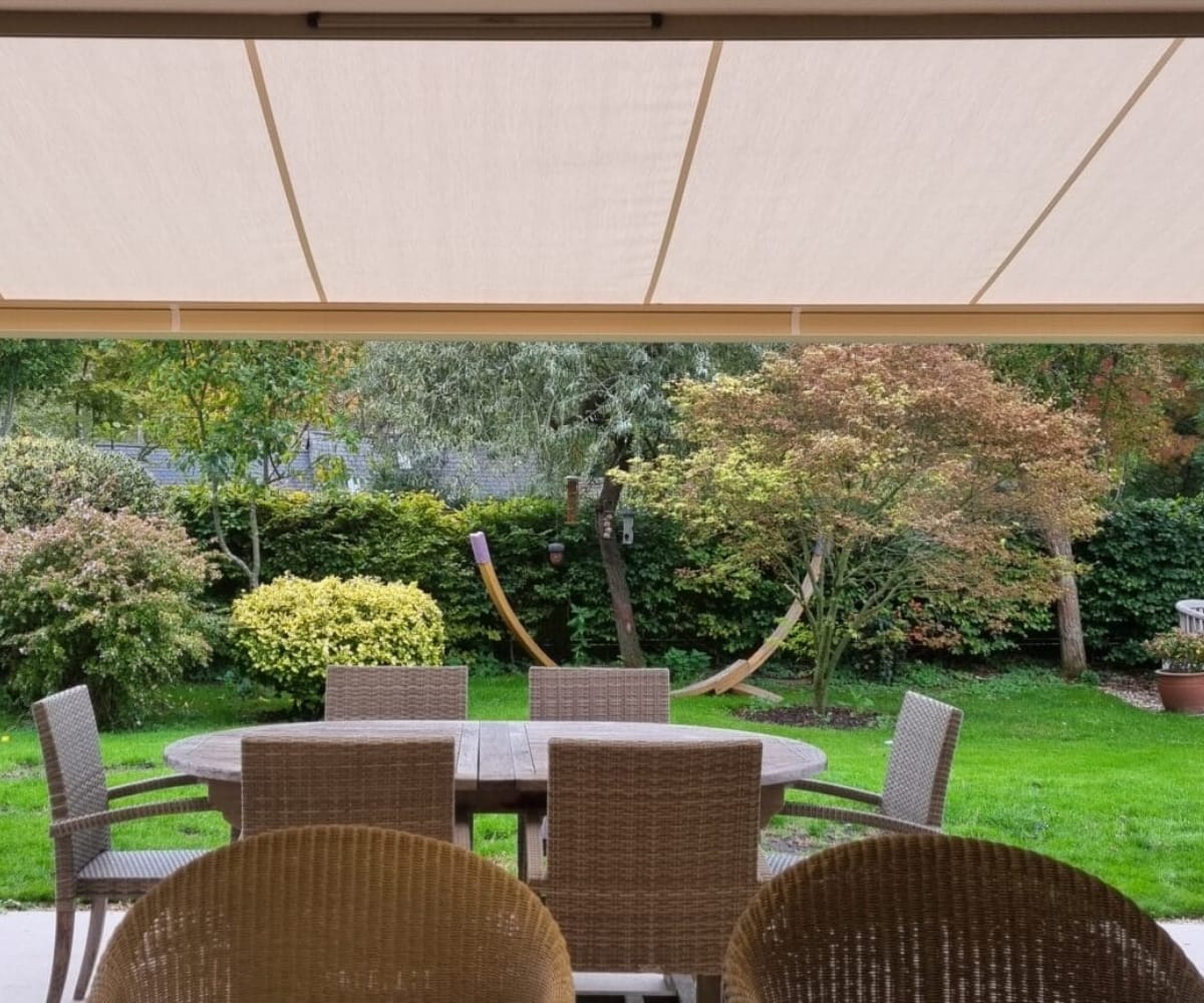 retractable awning or veranda: View from beneath a retractable awning overlooking a garden dining area with outdoor furniture