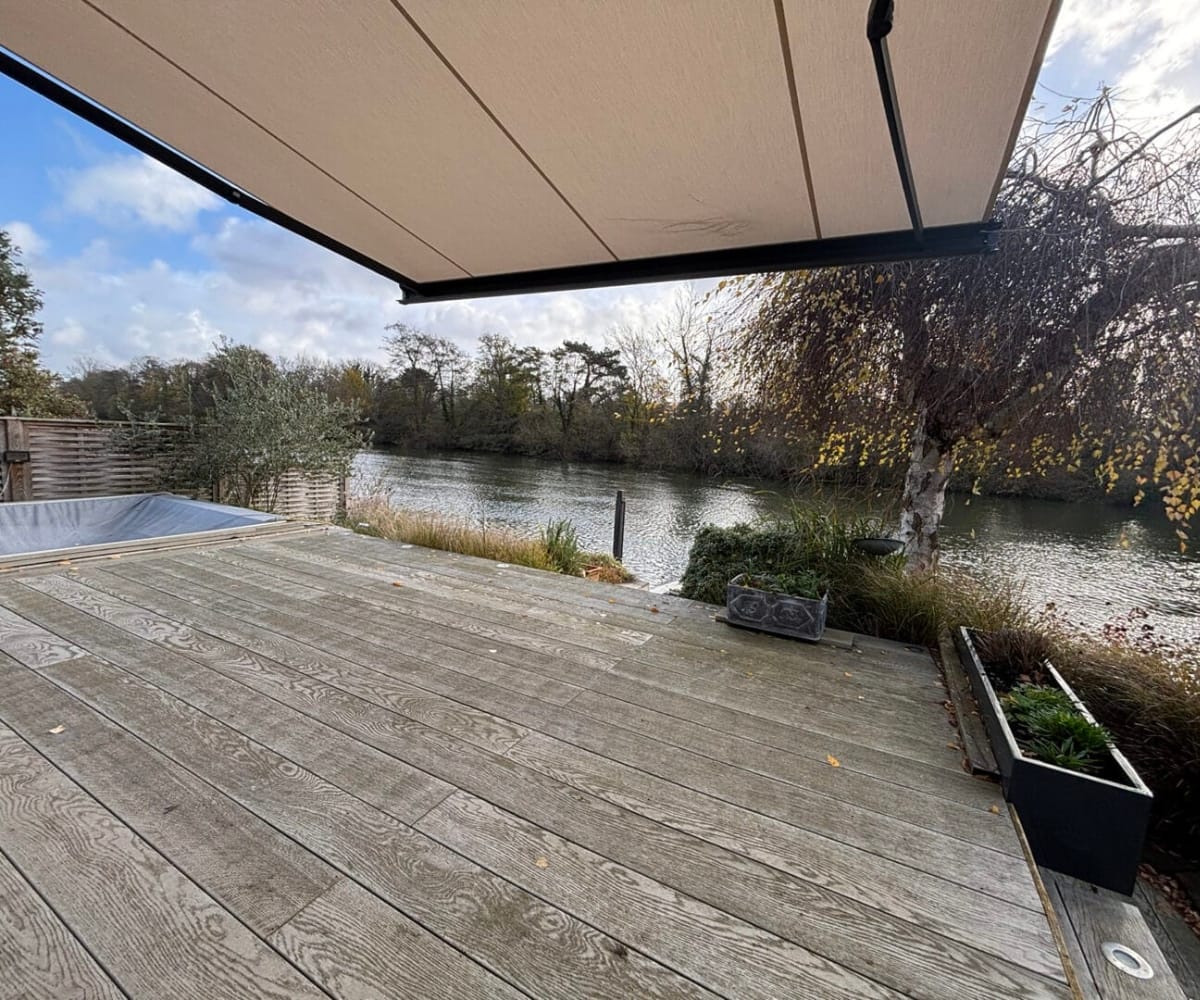 When to install a garden awning: Outdoor wooden decking beside a river with a retractable awning extended overhead, showing an installed garden awning in use.
