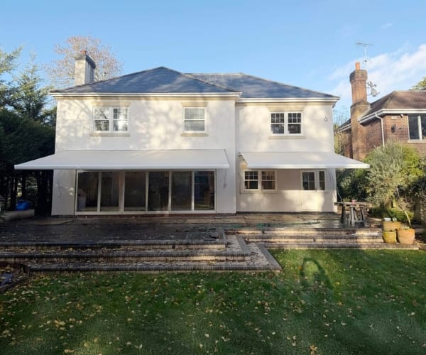 seasonal awnings inline image: Rear view of a large white house with two extended awnings providing shade over a patio and terrace area.