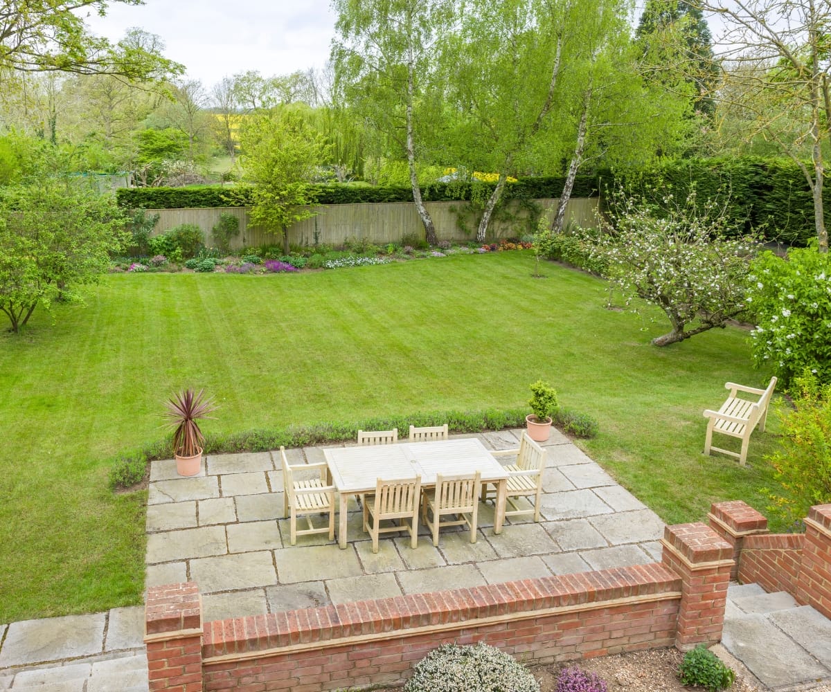 Awning zones: stone patio dining area leading onto large lawn with mature trees and landscaped garden borders