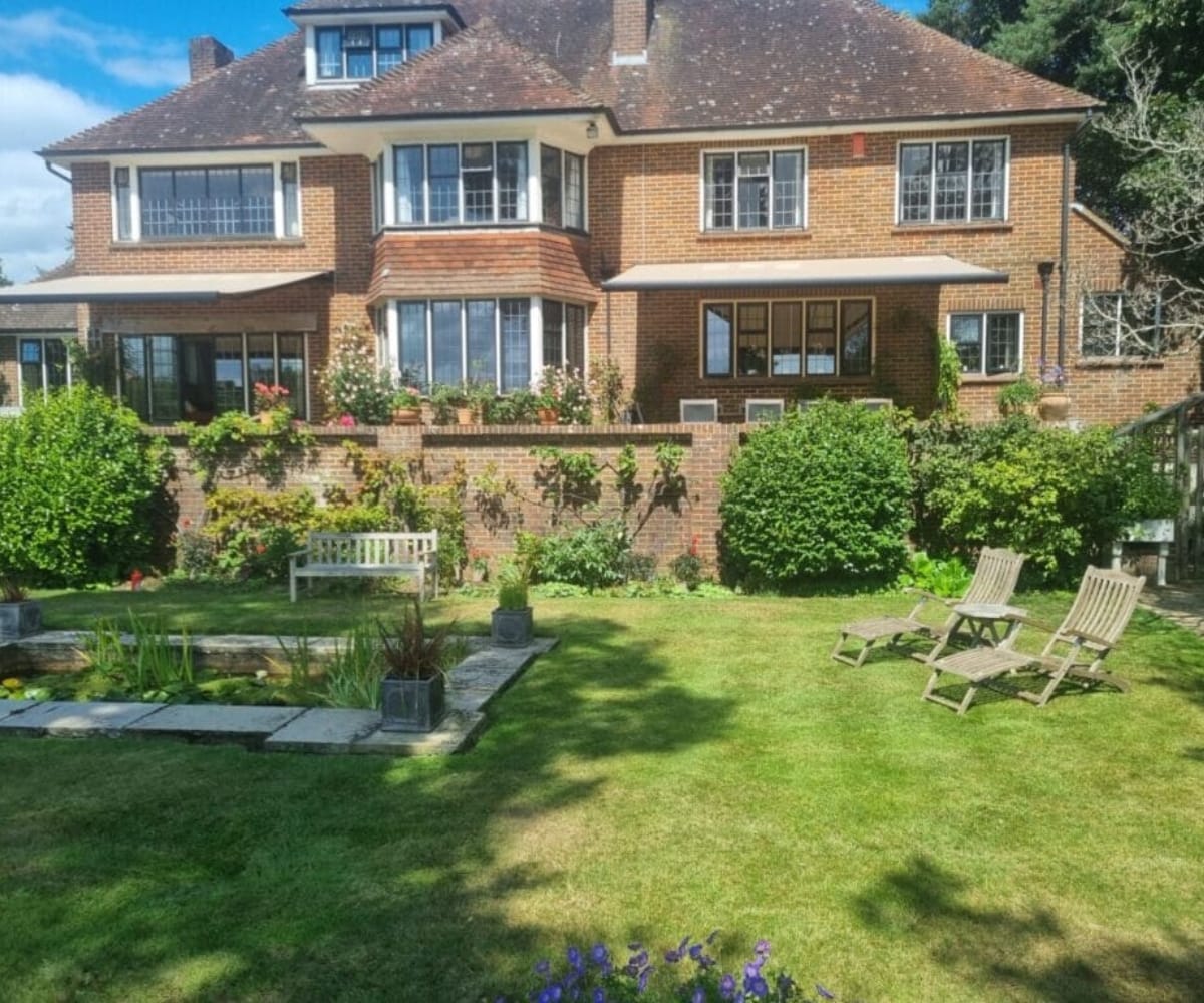 Awnings for patios: brick home with retractable patio awnings overlooking landscaped garden lawn and outdoor seating area