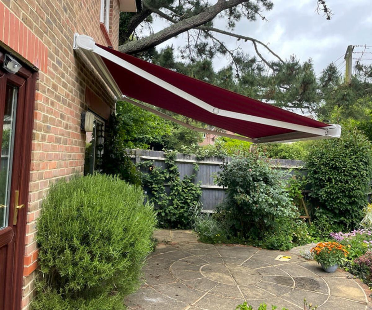 Garden rewilding – Side view of a red retractable awning above a patio in a leafy garden.