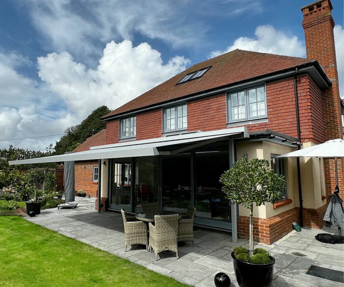 UV protection awnings: An awning installed by the Great British Awning and Blind Company on a red-brick house, with clouds and blue sky above.